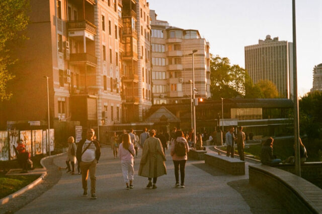 People walking on a wide sidewalk in a city near high rise buildings.